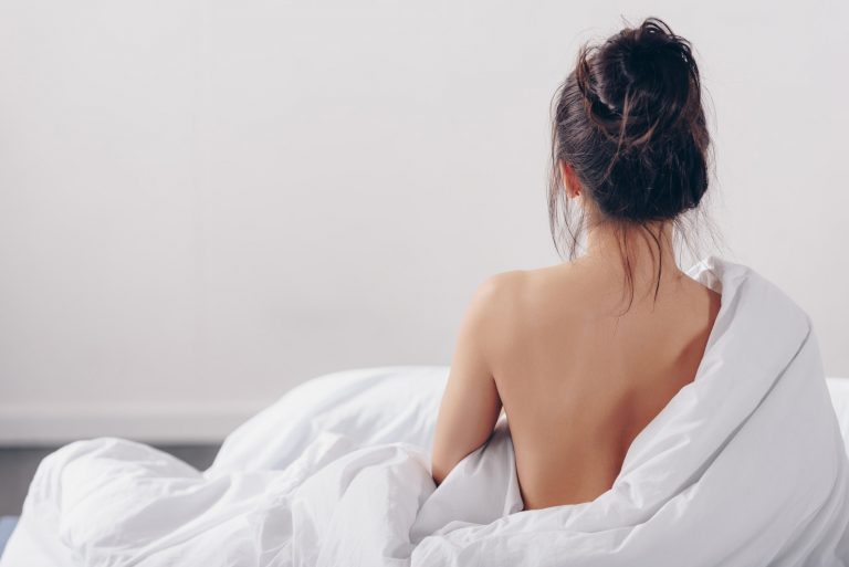 back view of nude woman sitting in bed