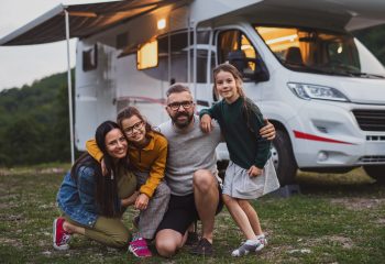 Happy family looking at camera outdoors at dusk, caravan holiday trip