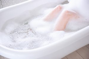 Womens delicate legs in white, fluffy foam in the bathroom. The girl takes a bath. Relaxing weekend
